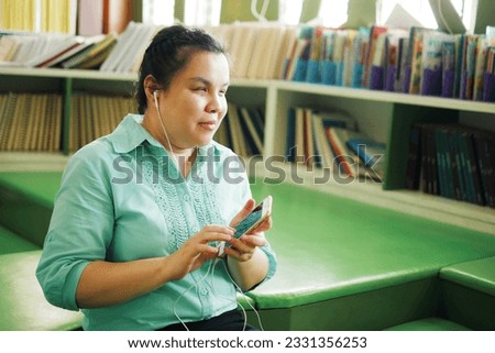 Portrait of Asian woman with blindness disability wearing earphones using smart phone with voice accessibility for persons with visual impairment disabilities in creative workplace library.