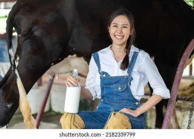 Portrait Of Asian Woman Dairy Farmer Holding Bottle Of Milk In Cowshed. Attractive Beautiful Female Agricultural Smile And Look At Camera After Milking Cow With Feel Proud At Livestock Farm Industry.