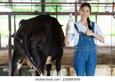 Portrait Of Asian Woman Dairy Farmer Holding Bottle Of Milk In Cowshed. Attractive Beautiful Female Agricultural Smile And Look At Camera After Milking Cow With Feel Proud At Livestock Farm Industry.