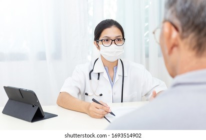 Portrait Of Asian Woman Doctor Wear Protection Face Mask Showing A Patient Some Information On Digital Tablet Clip Board, Patient Listen To Specialist Doctor In Clinic Office. Epidemic Protection.