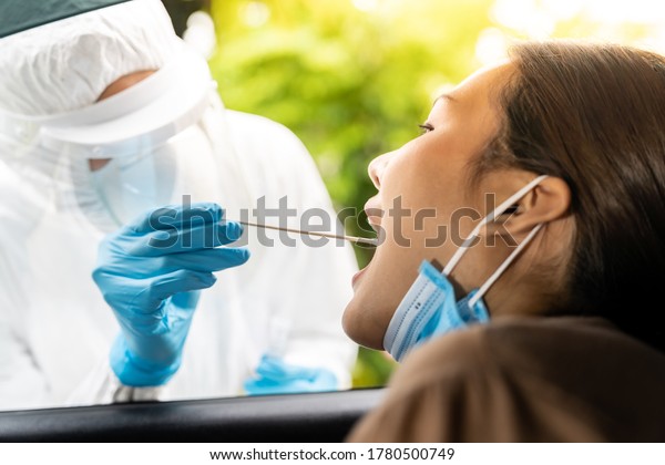 Portrait of asian woman\
drive thru coronavirus covid-19 test by medical staff with PPE suit\
by throat swab. New normal healthcare drive thru service and\
medical concept.