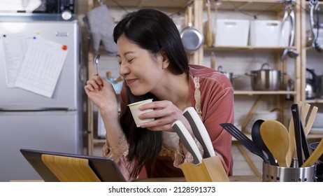 Portrait Asian Woman Is Having Delicious Yogurt With Contented Facial Expression While Playing And Binge Watching Dramas On Her Tablet.