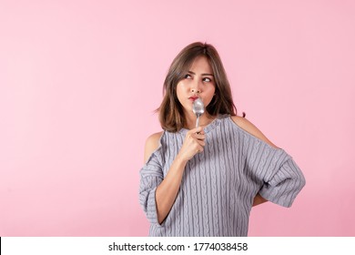 Portrait Of An Asian Woman Holding A Spoon And Fork In His Hand. She Is Choosing A Food Menu. Shot Of The Studio. 
Separately On The Pink Background.