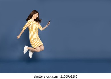 Portrait Of Asian Woman Jumping And Using Mobile Phone Application Isolated Over Blue Background, Asian Thai Model