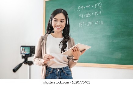 Portrait Of Asian Woman Live Teaching Video Camera. Influencer Teacher Girl With Gadget In School Math Classroom Over Blackboard Background Online Marketing Virtual Vlog Blogger Business In Quarantine