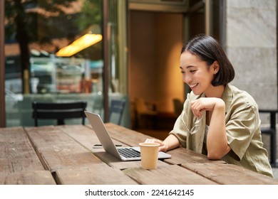 Portrait of asian woman looking at laptop, video chat, talking with someone via computer camera, sitting in cafe and drinking coffee, online meeting. - Powered by Shutterstock