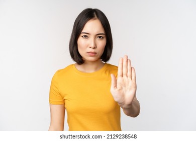 Portrait Of Asian Woman Looking Serious And Angry, Showing Stop Prohibit Gesture, Taboo Sign, Forbidding Smth, Standing In Yellow Tshirt Over White Background