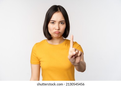 Portrait of asian woman looking serious and angry, showing stop prohibit gesture, taboo sign, forbidding smth, standing in yellow tshirt over white background - Shutterstock ID 2130545456