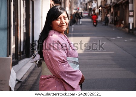 Portrait of an Asian woman with pink kimono dress on a blurred narrow street of Kyoto perecture