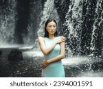 Portrait of Asian woman posing near the waterfall. Nature and environment concept. Travel lifestyle. Attractive woman wearing light blue dress. Copy space. Yeh Bulan waterfall in Bali, Indonesia