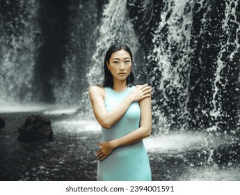 Portrait of Asian woman posing near the waterfall. Nature and environment concept. Travel lifestyle. Attractive woman wearing light blue dress. Copy space. Yeh Bulan waterfall in Bali, Indonesia