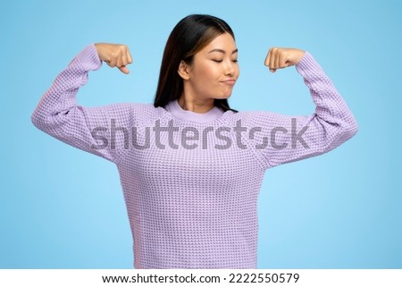 Portrait of asian woman raising arms showing biceps as metaphor of female power and independence, feminism. Indoor studio shot isolated on blue background  Foto stock © 