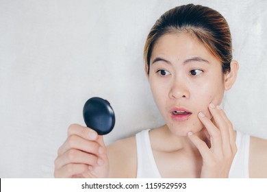 Portrait Of Asian Woman Shocked When She Saw The Problem Of Acne And Scar On Her Face By The Mini Mirror. Conceptual Shot Of Acne And Problem Skin On Female Face.