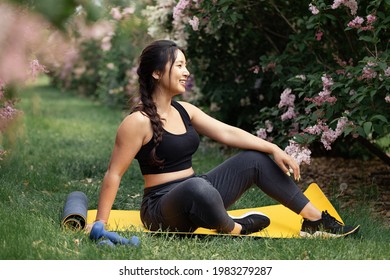 Portrait of an Asian woman sitting on a yoga man and is surrounding by spring bloom. She is smiling and wearing active wear.  - Powered by Shutterstock