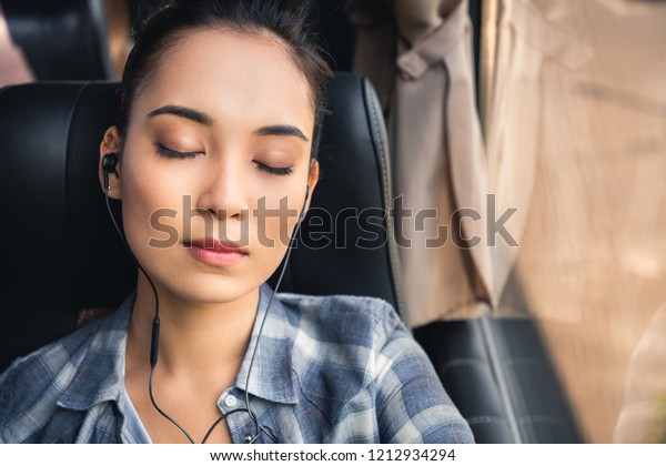 portrait of asian woman sleeping and\
listening music in earphones during trip on travel bus\
