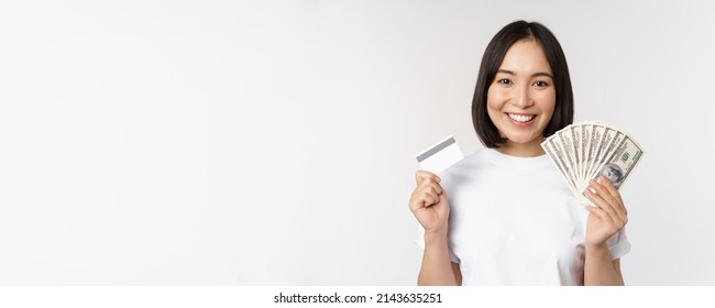 Portrait Of Asian Woman Smiling, Holding Credit Card And Money Cash, Dollars, Standing In Tshirt Over White Background