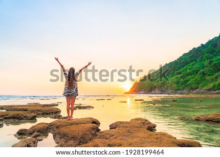 Portrait asian woman stand on the rock at sunset around beach sea ocean in travel vacation trip