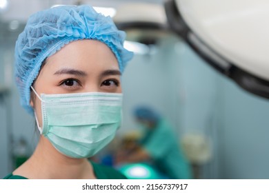 Portrait Of Asian Woman Surgeon With Medical Mask Standing In Operation Theater At A Hospital. Team Of Professional Surgeons. Healthcare, Emergency Medical Service Concept