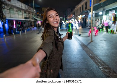 Portrait of Asian woman traveler hold boyfriend's hand, walk on street. Young man and woman tourist travel in city spend time on vacation together and drink bottle of beer at dark night on the road. - Powered by Shutterstock