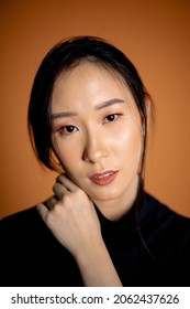 Portrait Asian Woman Wearing Black Turtle Neck Shirt With Studio Lighting , Brown Orange Background.