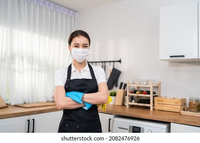 Portrait of Asian young cleaning service woman worker working in house. Beautiful girl housekeeper cleaner wear mask, hold feather duster and smile, looking at camera after doing housework or chores.