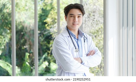 Portrait Of Asian Young Doctor Standing, Cross Arms Posing Near Windows In Medical Office. Ratio 16:9