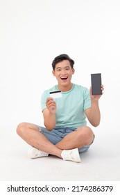 Portrait Of Asian Young Handsome And Cheerful Man, Sitting And Use Credit Card On Smart Phone, Isolated On White Background. Concept Of Confident Male Student Paying For Online Shopping.