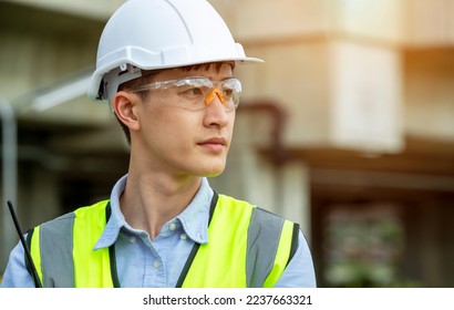 Portrait of Asian young handsome confident engineer wearing safety goggles and white hard hat in construction site outdoors - Powered by Shutterstock