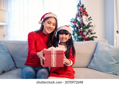 Portrait Of Asian Young Little Young Daughter Open Gift Box From Mom. Happy Family, Little Kid Feel Happy And Excited For Surprise From Mother Ready To Celebrate Christmas Together And Look At Camera.