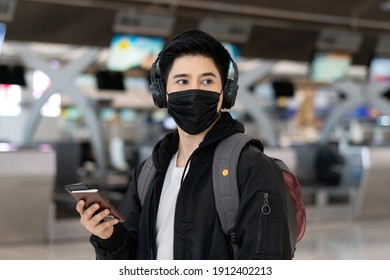 Portrait Of Asian Young Man Wearing Protective Mask With Backpack And Listening To Music At Airport. Tourist Passenger Travel By Airline Service During Covid19 Epidemic At Airport Terminal. Copy Space