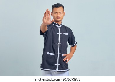 Portrait Of Asian Young Man Wearing Taekwondo Kimono Doing Stop Motion With Palm Isolated On Gray Background