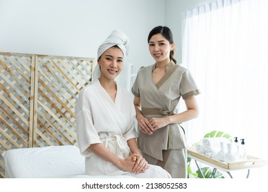 Portrait of Asian young masseuse woman and client looking at camera. Attractive beautiful girl sit on massage table with female worker after doing physiotherapy for skin, body care in spa beauty salon - Powered by Shutterstock