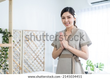 Portrait of Asian young masseuse woman smiling and looking at camera. Attractive beautiful worker standing near massage table with confidence after serve physiotherapy to customer in spa beauty salon.