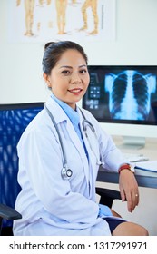 Portrait Of Asian Young Neurologist In Lab Coat Sitting In Chair At Her Workplace At Office