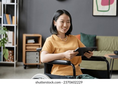 Portrait of Asian young woman using wheelchair smiling at camera and holding tablet in office, copy space - Powered by Shutterstock