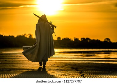 Portrait des Mörders in weißem Kostüm mit dem Schwert am Meer. Er posiert bei schönem Sonnenuntergang am Meer. Gelbes, weiches Licht.