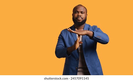 Portrait of assertive BIPOC man asking for timeout, doing hand gestures, feeling fatigued. Unhappy person doing vehement pause sign gesturing, wishing for break, studio background, camera B