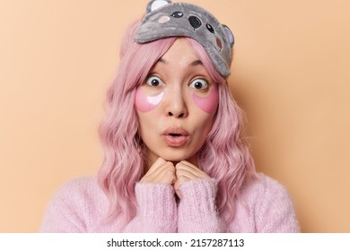 Portrait Of Astonished Asian Woman Keeps Hands Under Chin Wears Blindfold And Casual Jumper Applies Beauty Patches Under Eyes To Remove Wrinkles Reacts To Shocking News Isolated Over Brown Wall