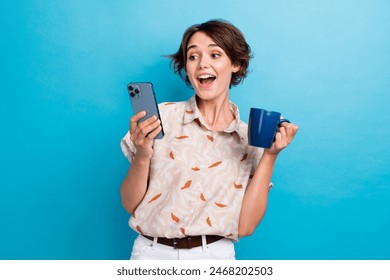 Portrait of astonished nice girl hold coffee mug use smart phone texting isolated on blue color background - Powered by Shutterstock