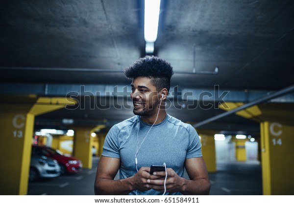 Portrait of athlete man using\
mobile phone and listening to the music in the underground car\
parking.