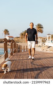 Portrait Of Athletic 60-years Old Man Walking Together With His Dog Jack Russell Terrier By The Sea.