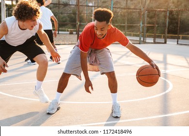 Portrait of athletic american and caucasian men playing basketball at the playground outdoor during summer sunny day
