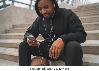 Portrait of an athletic man using his mobile phone on a break from training while sitting on concrete stairs. Sport and health concept.