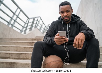 Portrait of an athletic man using his mobile phone on a break from training while sitting on concrete stairs. Sport and health concept.