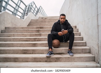 Portrait of an athletic man using his mobile phone on a break from training while sitting on concrete stairs. Sport and health concept.