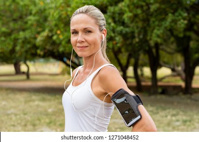 Portrait Of Athletic Mature Woman Resting After Jogging. Beautiful Mid Blonde Woman Running At Park On A Sunny Day. Female Runner Listening To Music While Jogging And Looking At Camera.