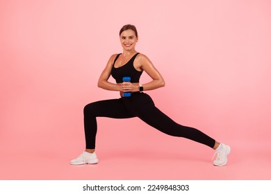 Portrait Of Athletic Young Woman Training With Dumbbells In Studio, Beautiful Sporty Female Making Core Rotation Exercise With Light Weights And Smiling At Camera While Posing Over Pink Background