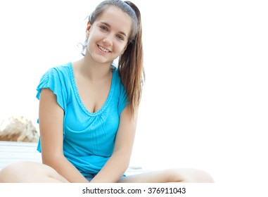 Portrait of attractive adolescent girl sitting by the sea, smiling on a summer holiday against the sky, outdoors. Teenager travel lifestyle, healthy relaxing. Young woman wearing by the ocean.