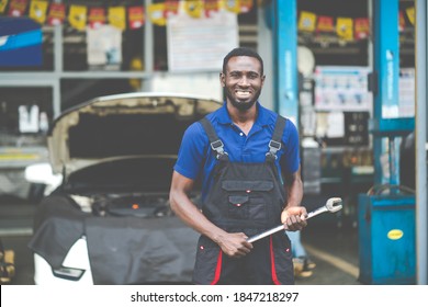 Portrait of attractive African man smiling to the camera and big wrench tools in hand. Expertise mechanic working in automobile repair garage. 