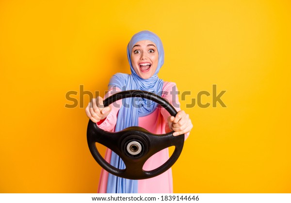 Portrait of attractive amazed cheerful glad\
excited muslimah lady wearing hijab driving invisible car isolated\
shine yellow color\
background